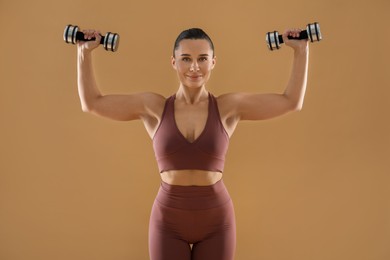 Photo of Woman exercising with dumbbells on beige background