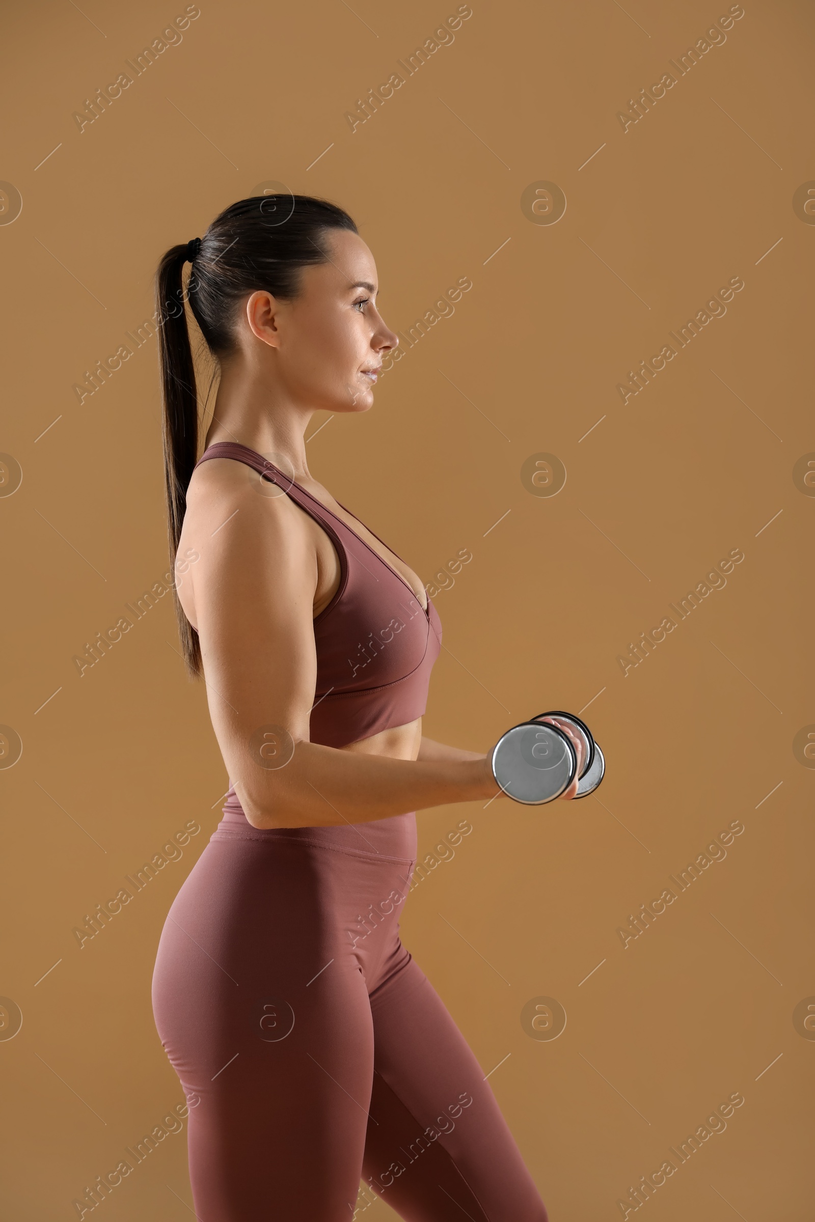 Photo of Woman exercising with dumbbells on beige background