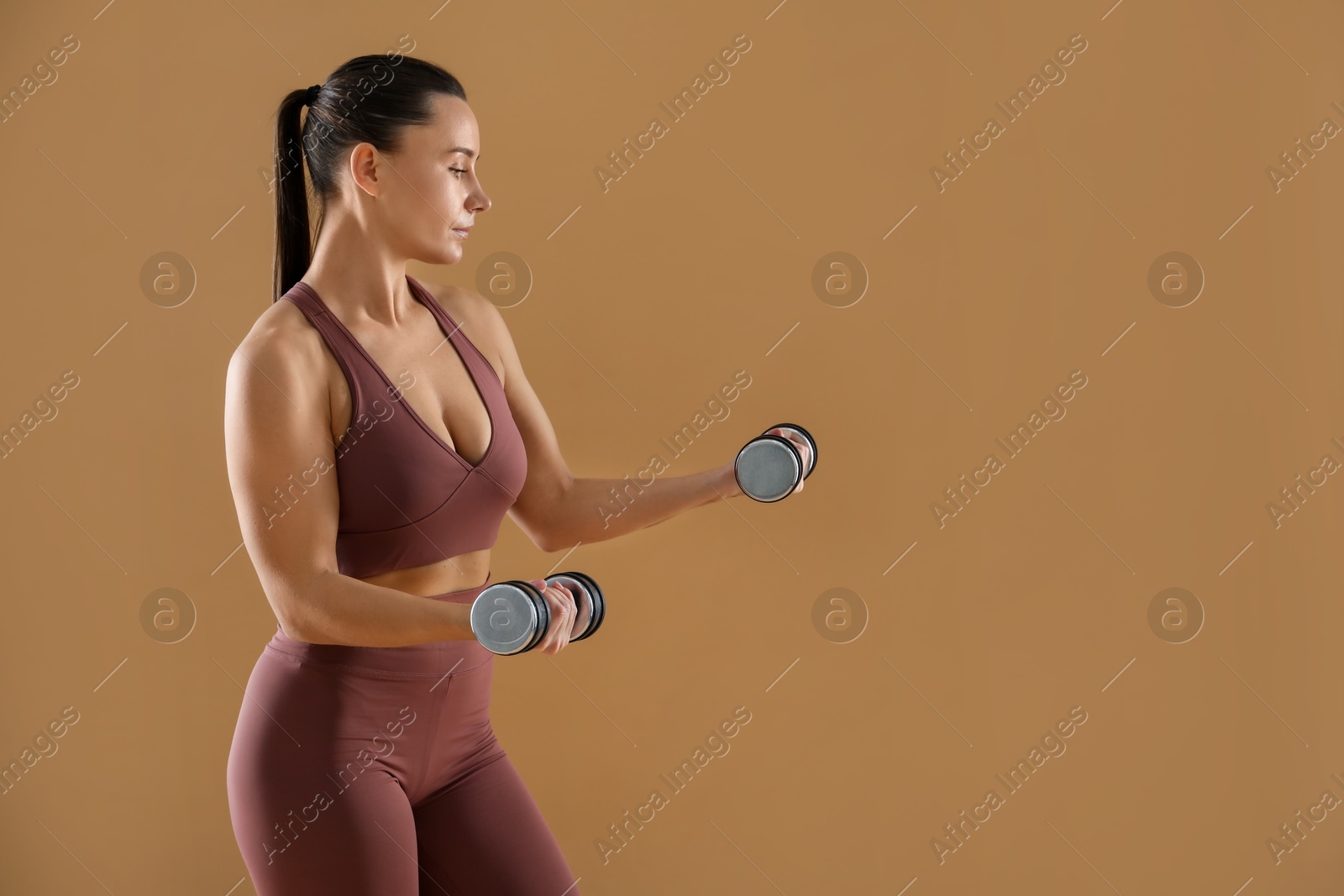 Photo of Woman exercising with dumbbells on beige background, space for text