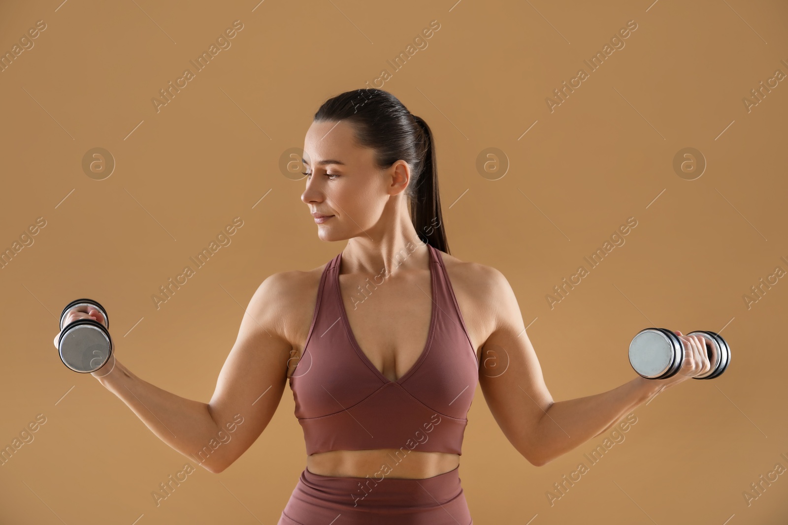 Photo of Woman exercising with dumbbells on beige background