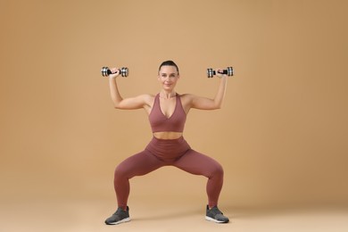 Photo of Woman exercising with dumbbells on beige background