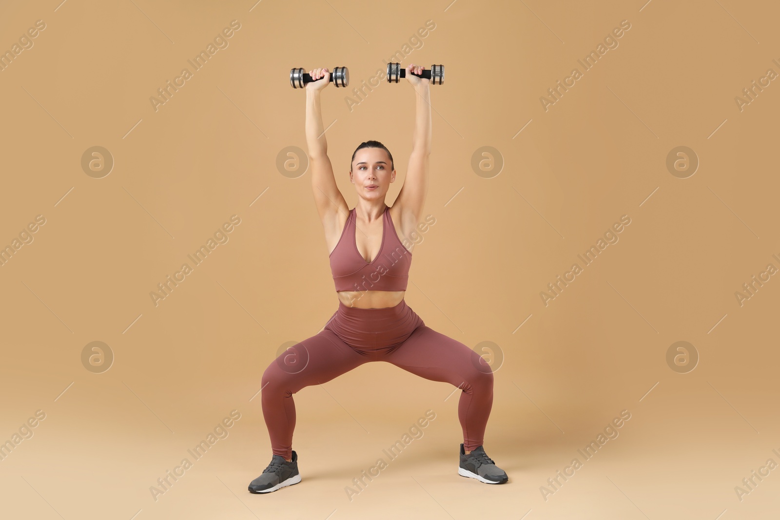 Photo of Woman exercising with dumbbells on beige background