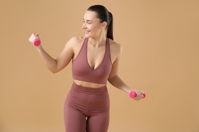 Photo of Woman exercising with dumbbells on beige background