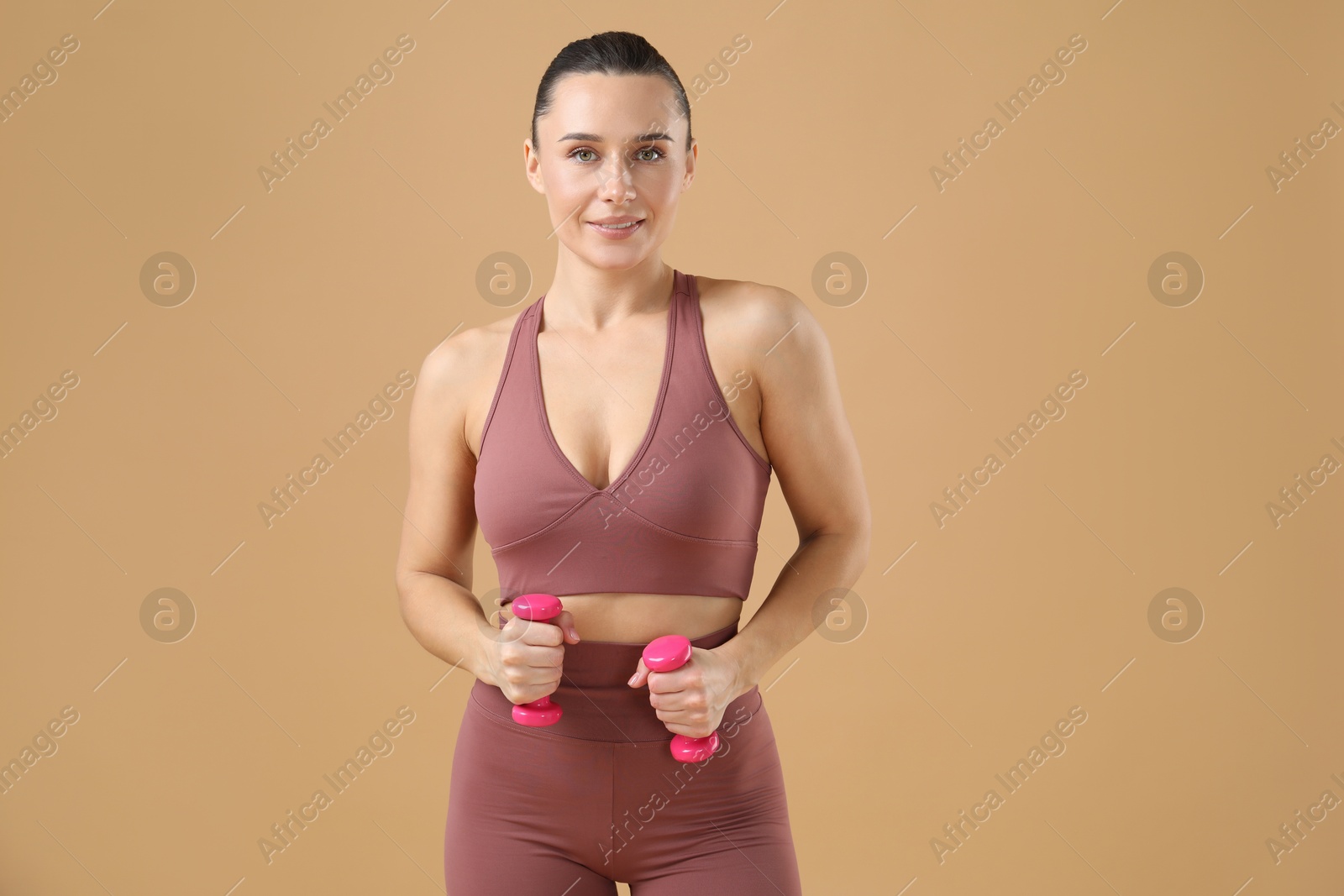 Photo of Woman exercising with dumbbells on beige background