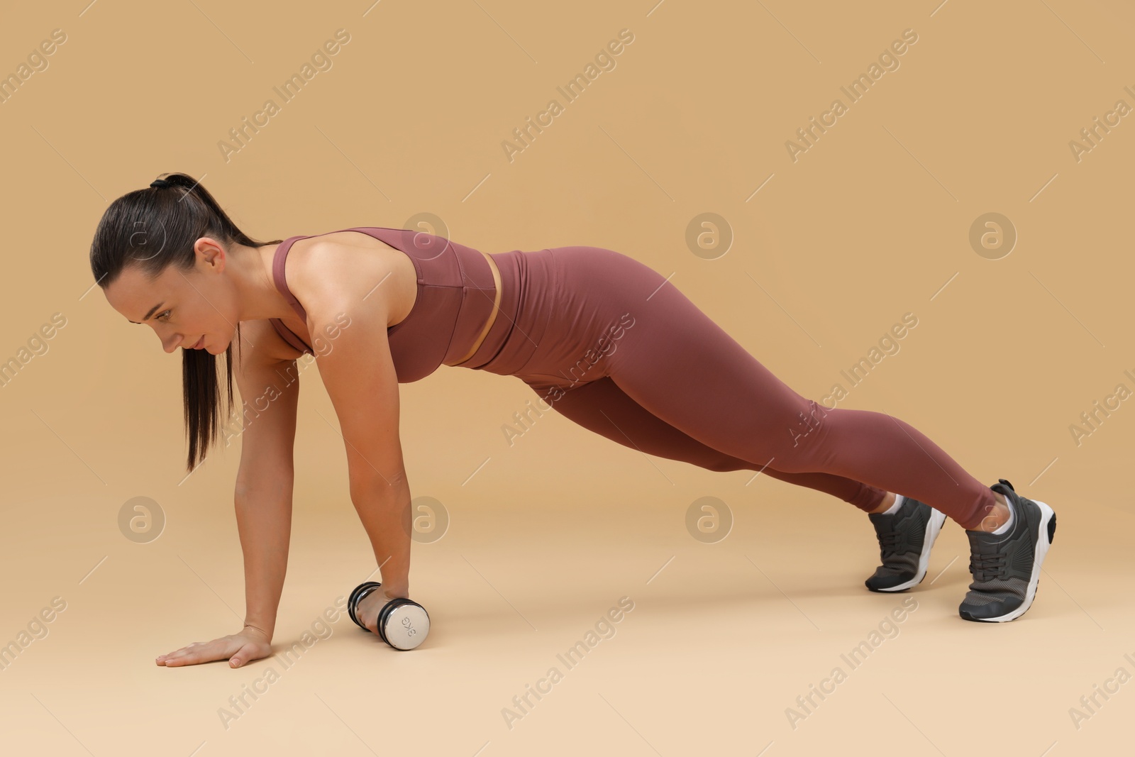 Photo of Woman exercising with dumbbell on beige background