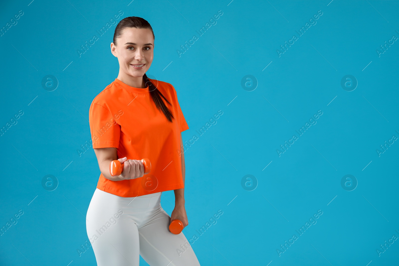 Photo of Woman exercising with dumbbells on light blue background, space for text