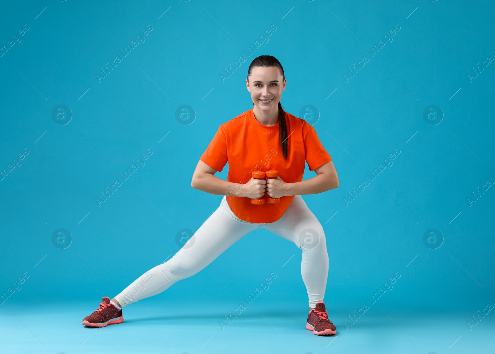 Photo of Woman exercising with dumbbells on light blue background