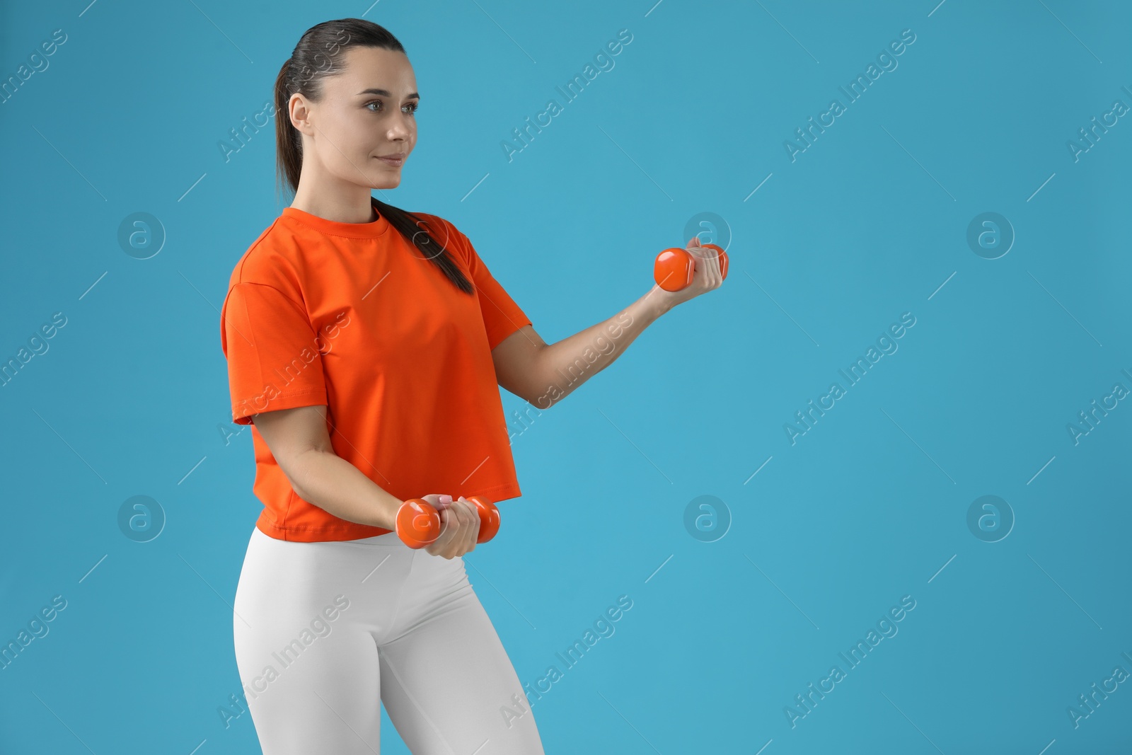 Photo of Woman exercising with dumbbells on light blue background, space for text