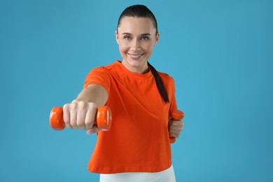 Photo of Woman exercising with dumbbells on light blue background