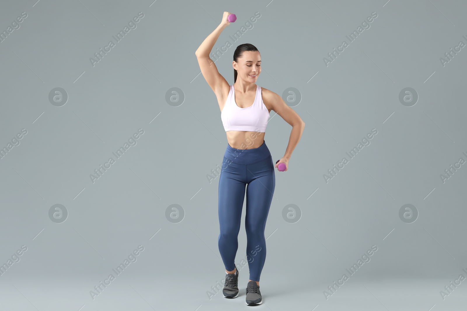 Photo of Woman exercising with dumbbells on light grey background