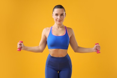 Photo of Woman exercising with dumbbells on orange background