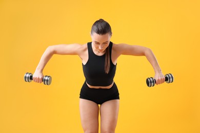 Photo of Woman exercising with dumbbells on orange background