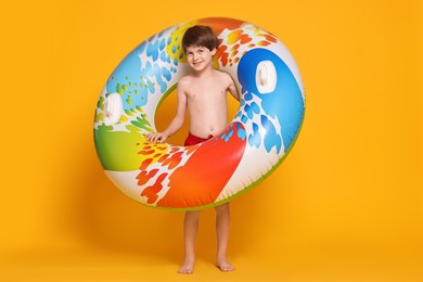 Photo of Little boy in beachwear with inflatable ring on orange background