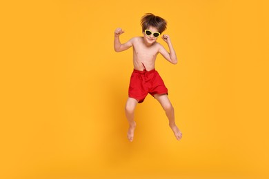 Photo of Little boy in beachwear jumping on orange background, space for text