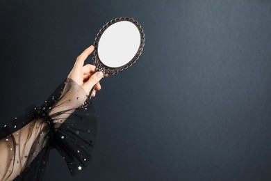 Woman holding vintage mirror on grey background, closeup. Space for text