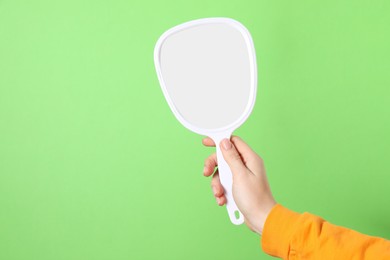 Woman holding mirror on green background, closeup. Space for text