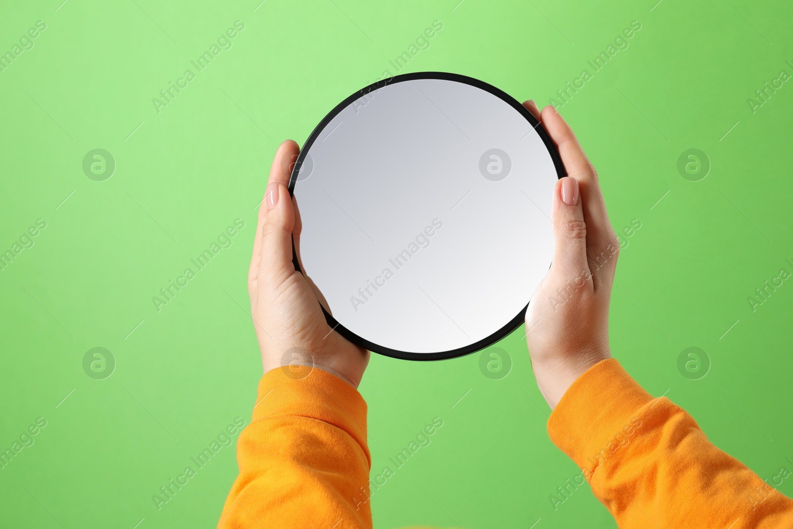 Photo of Woman holding round mirror on green background, closeup