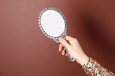 Photo of Woman holding vintage mirror on brown background, closeup