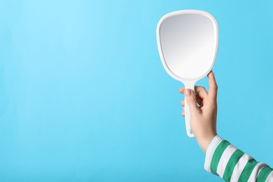 Woman holding mirror on light blue background, closeup. Space for text