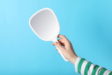 Photo of Woman holding mirror on light blue background, closeup