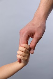 Father and child holding hands on grey background, closeup