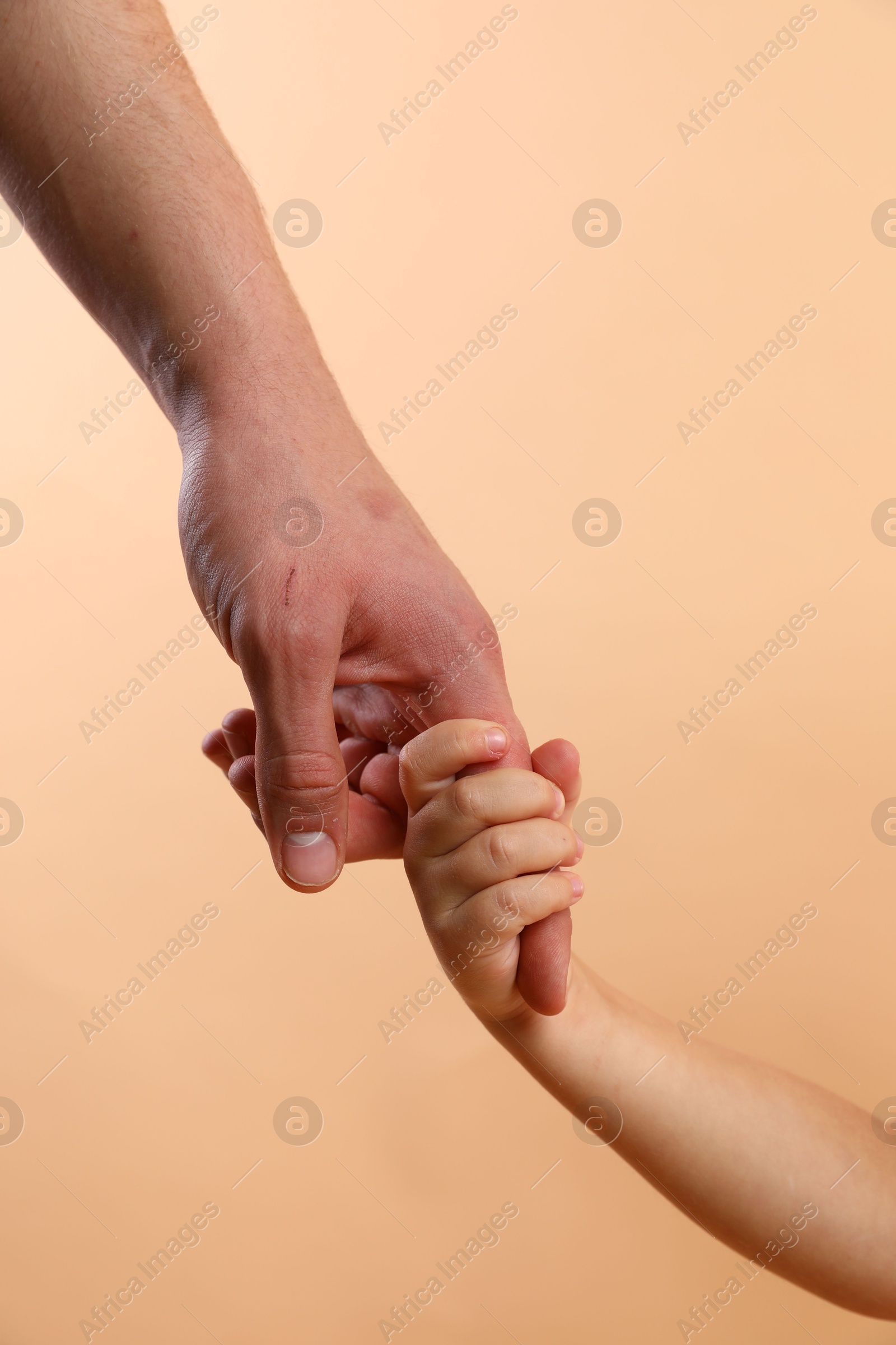 Photo of Father and child holding hands on beige background, closeup