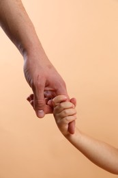 Father and child holding hands on beige background, closeup