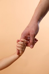 Photo of Father and child holding hands on beige background, closeup