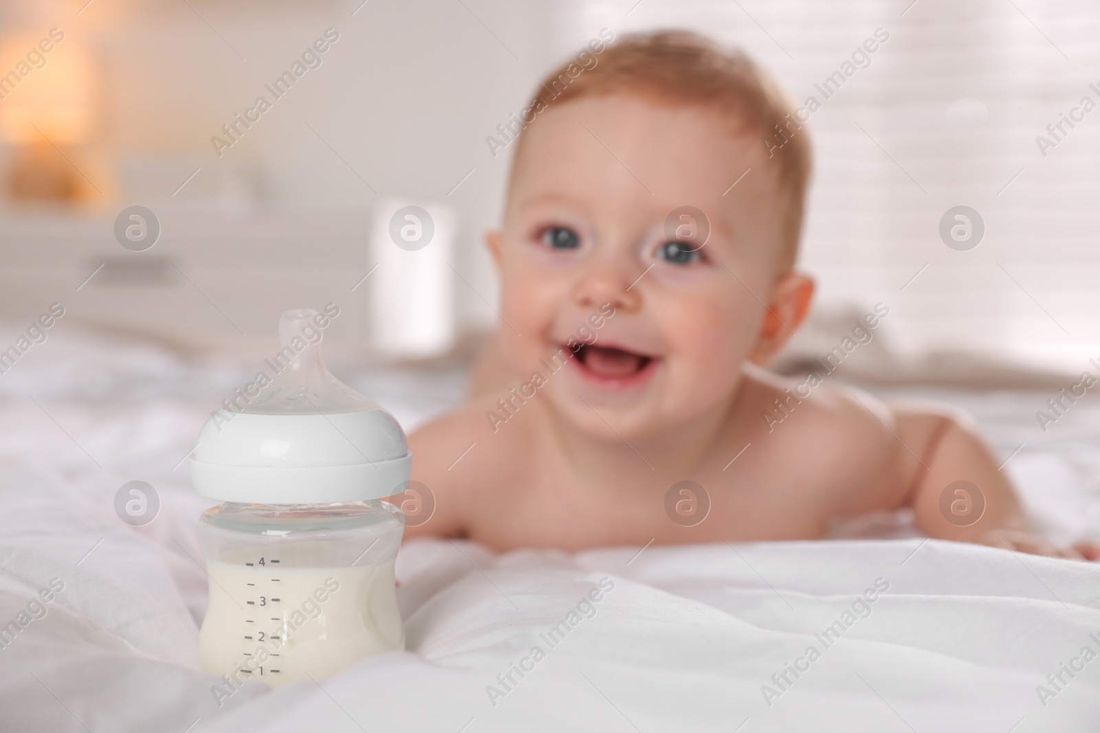 Photo of Cute little baby on bed indoors, focus on bottle of milk