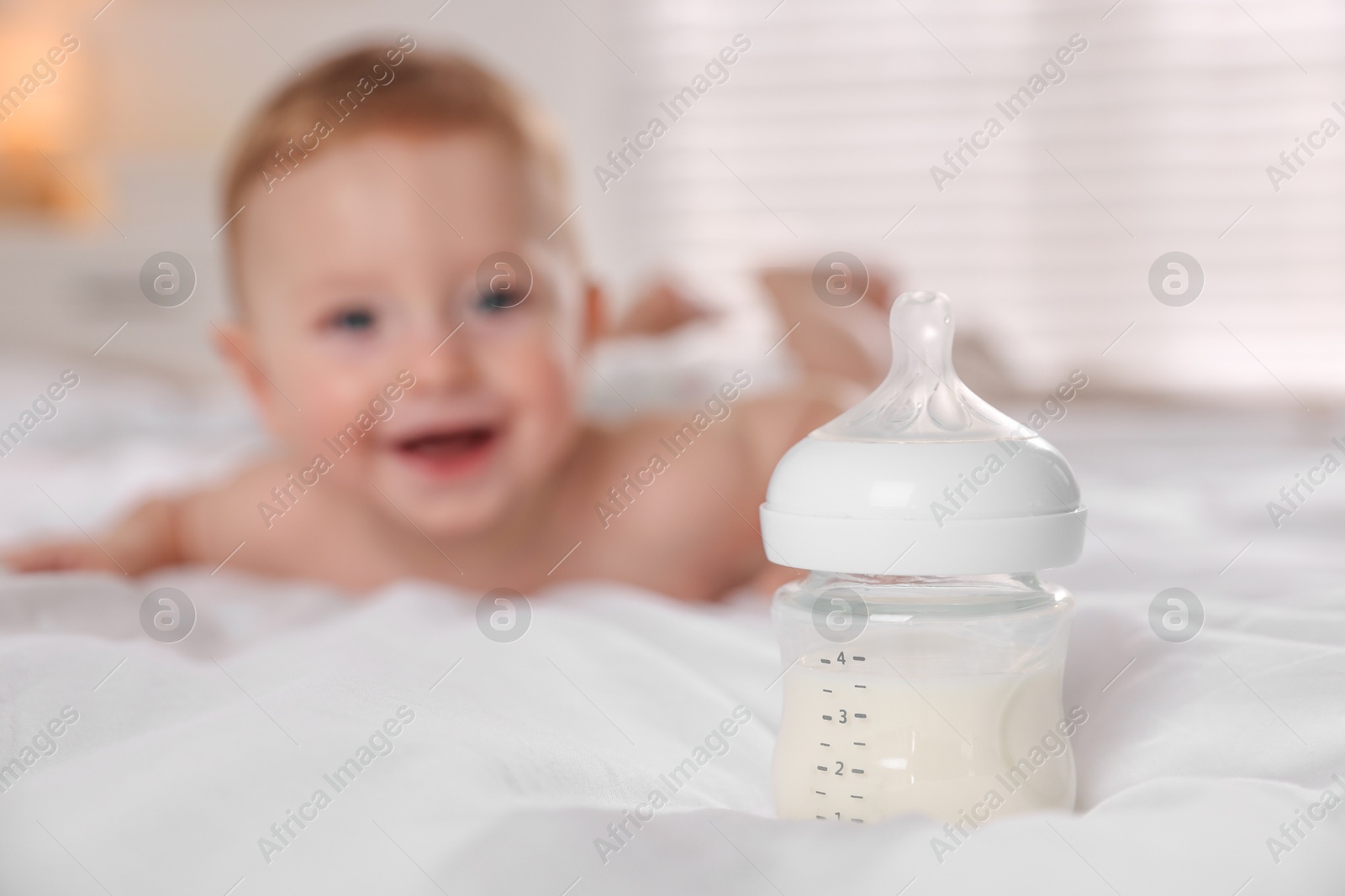 Photo of Cute little baby on bed indoors, focus on bottle of milk