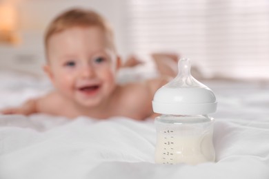 Photo of Cute little baby on bed indoors, focus on bottle of milk