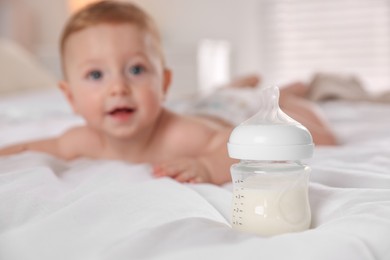 Photo of Cute little baby on bed indoors, focus on bottle of milk