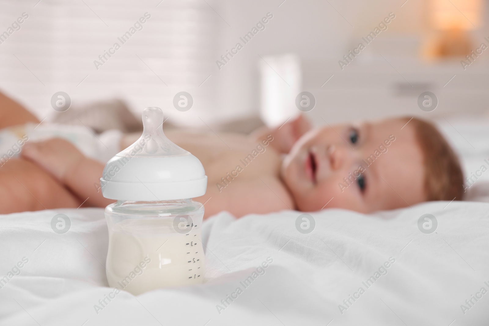 Photo of Cute little baby on bed indoors, focus on bottle of milk