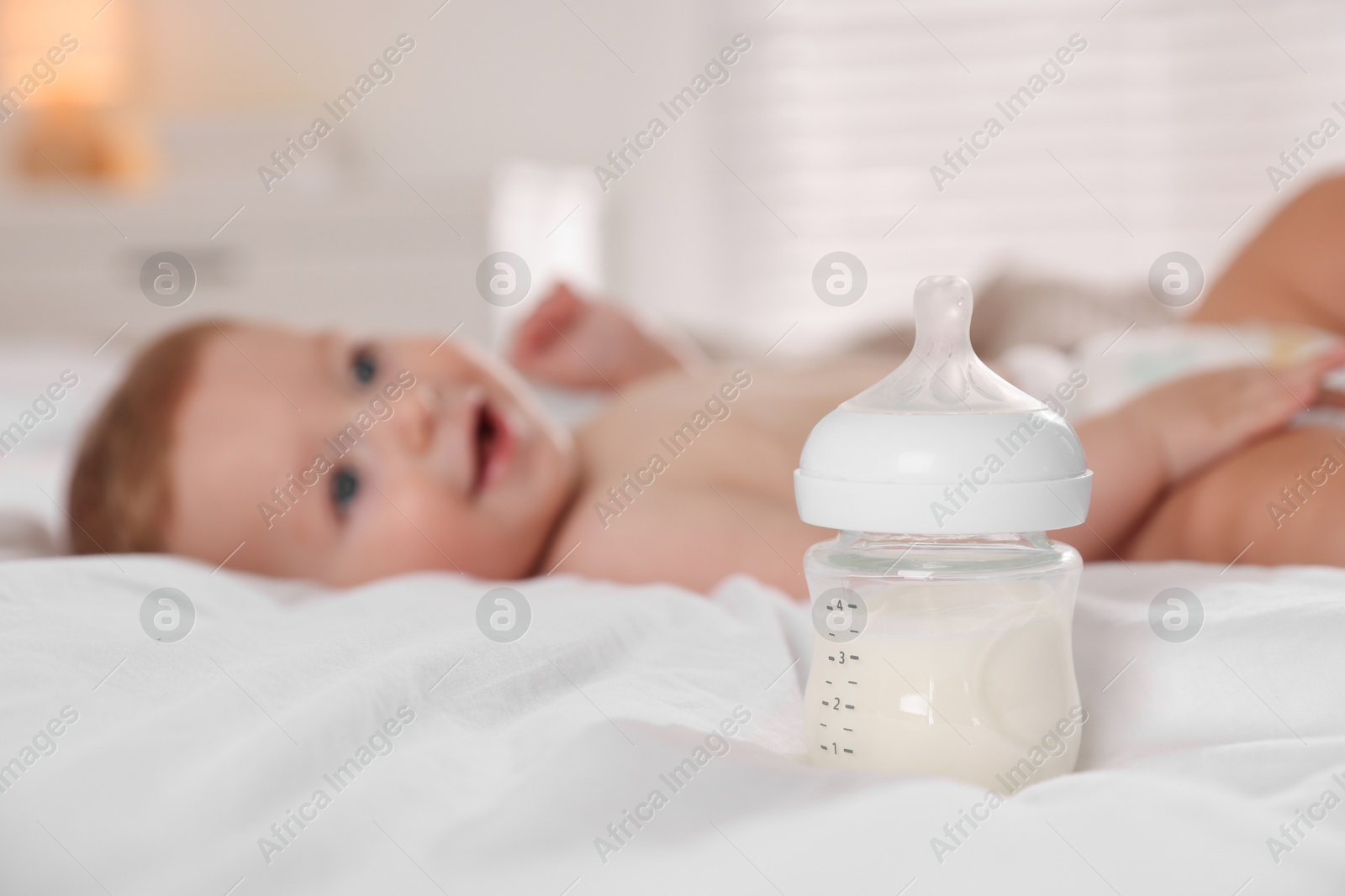 Photo of Cute little baby on bed indoors, focus on bottle of milk