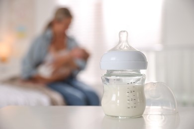 Photo of Mother holding her cute little baby indoors, focus on bottle with milk