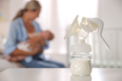 Photo of Mother holding her cute little baby indoors, focus on breast pump with milk