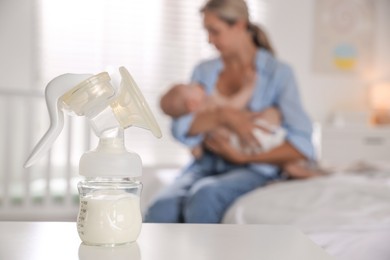 Photo of Mother holding her cute little baby indoors, focus on breast pump with milk