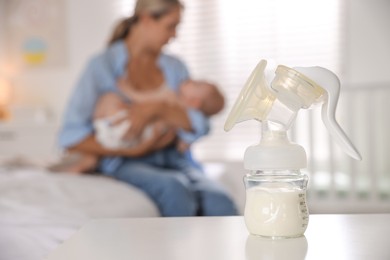 Photo of Mother holding her cute little baby indoors, focus on breast pump with milk