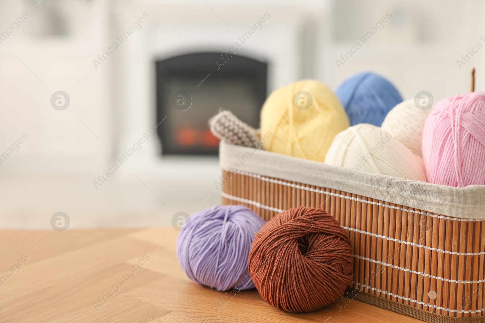 Photo of Colorful yarns and basket on wooden table indoors, closeup. Space for text