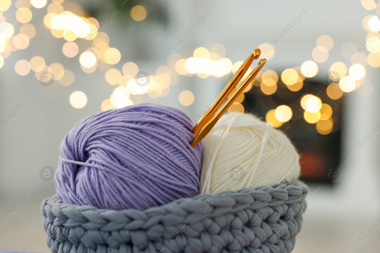 Photo of Basket with colorful yarns and crochet hooks against blurred lights, closeup