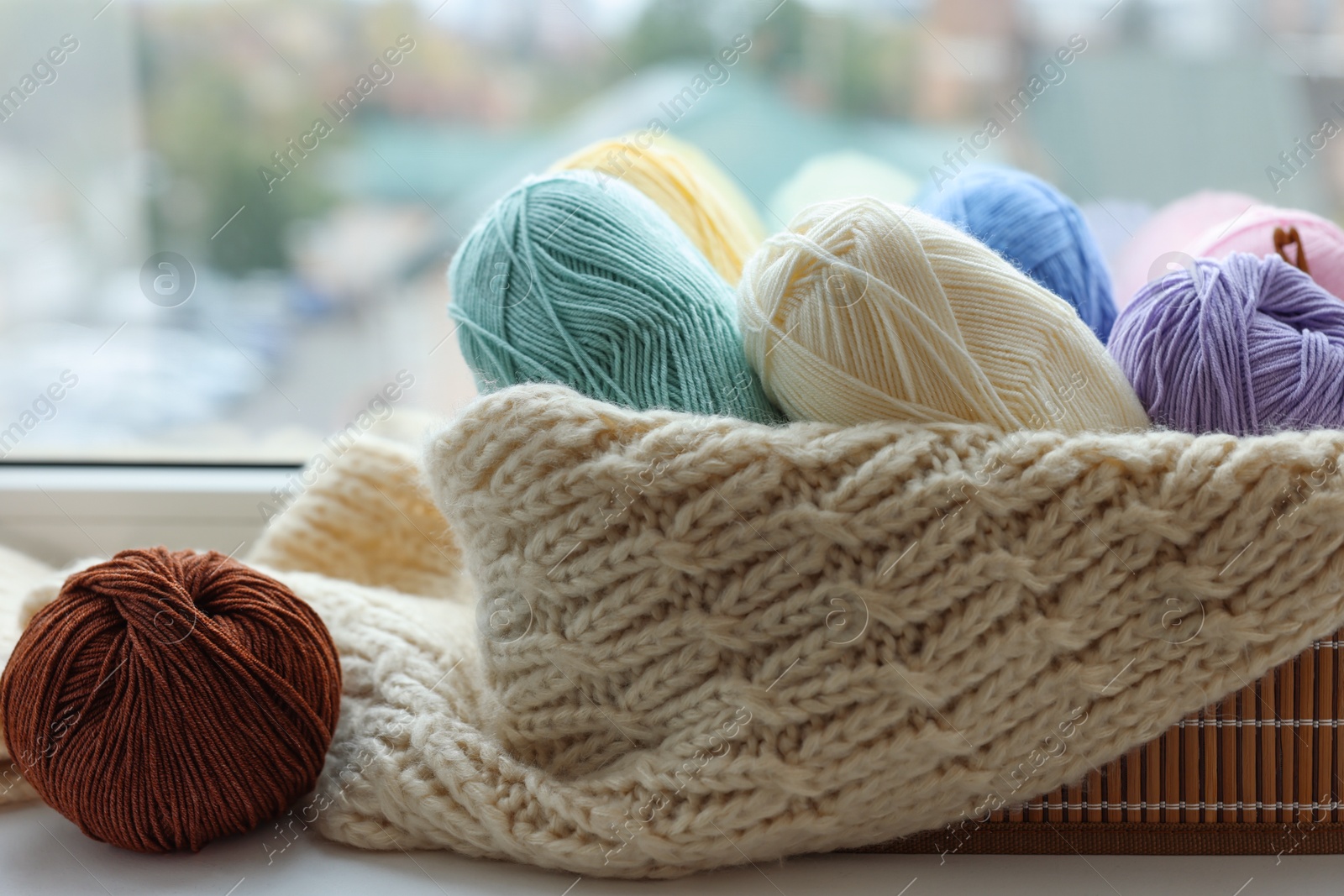 Photo of Many colorful yarns, sweater and basket on window sill