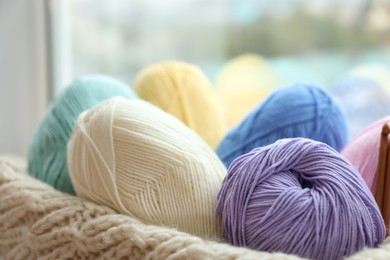 Photo of Many colorful yarns and sweater on blurred background, closeup