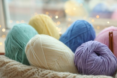 Photo of Many colorful yarns and sweater on blurred background, closeup