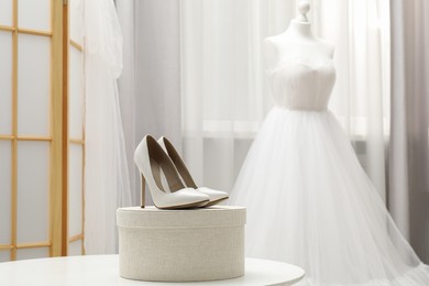 Photo of Beautiful wedding dress on mannequin and shoes in boutique, selective focus