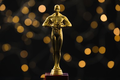 Photo of Golden trophy in shape of human figure on dark background with blurred lights