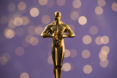 Photo of Golden trophy in shape of human figure on purple background with blurred lights