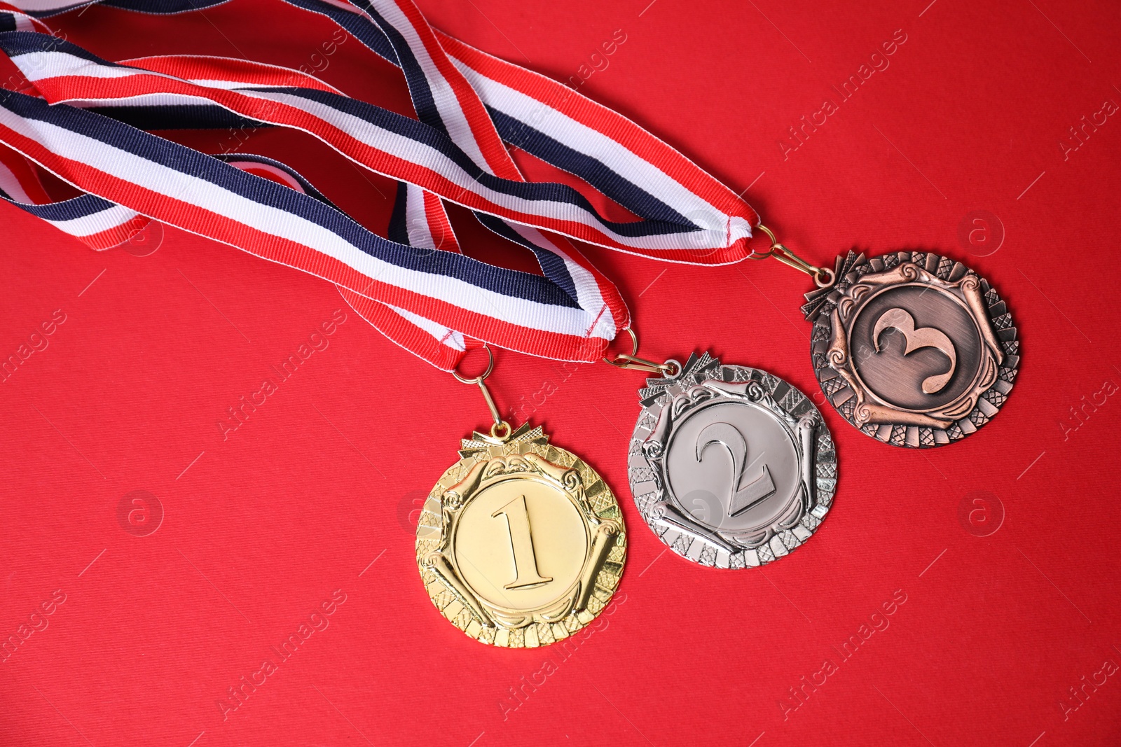 Photo of Golden, silver and bronze medals on red background, top view