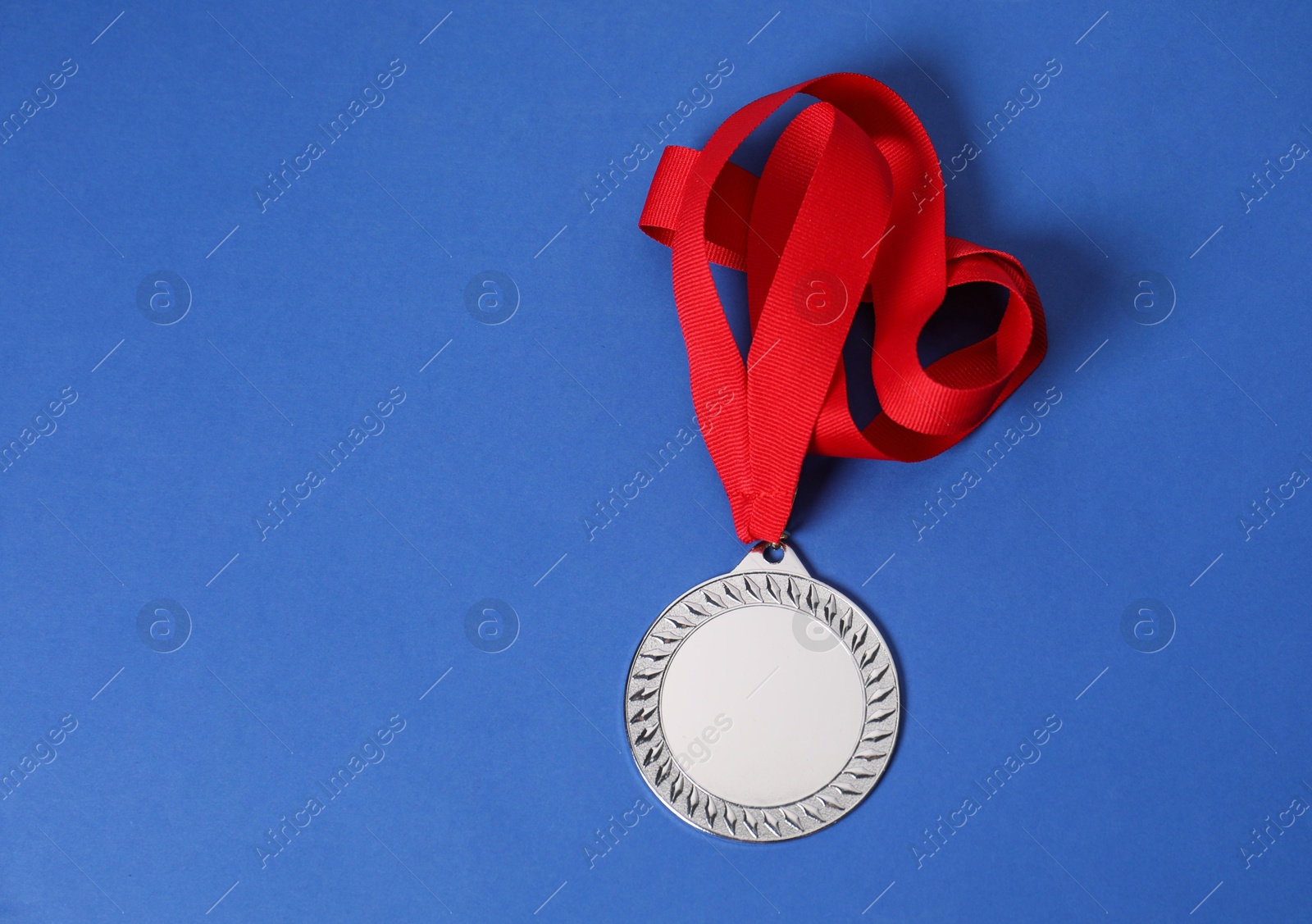 Photo of Silver medal with red ribbon on blue background, top view. Space for text