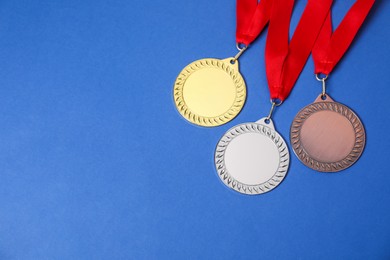 Photo of Golden, silver and bronze medals on blue background, top view. Space for text