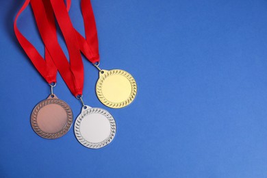 Photo of Golden, silver and bronze medals on blue background, top view. Space for text